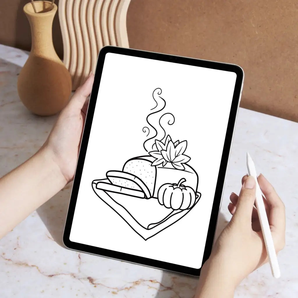 Person using a stylus to color on a tablet with an illustration of a fresh pumpkin loaf garnished with fall leaves and a mini pumpkin on a cloth napkin