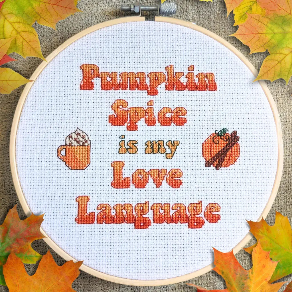 Embroidery hoop with 'Pumpkin Spice is my Love Language' text and fall-themed icons on a textured background with leaves.