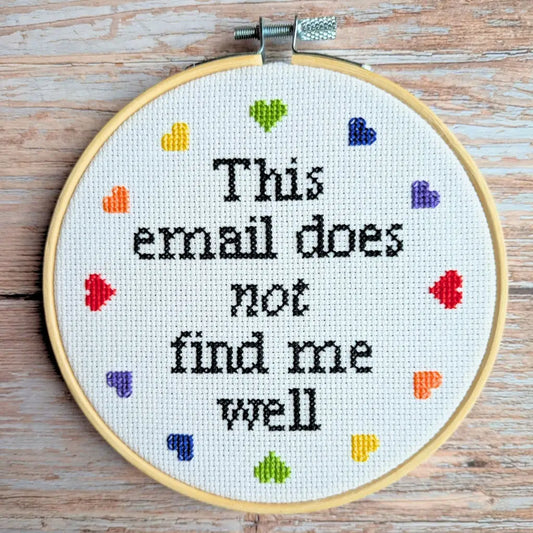 Embroidery hoop with cross-stitched text 'This email does not find me well' on a wooden surface.