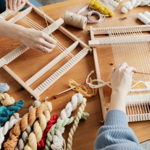 Two sets of hands work at small looms on a wood table