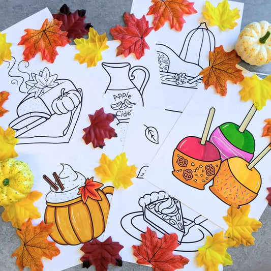 Printed coloring pages with autumn food-themed illustrations and mini pumpkins on a gray surface with fall leaves