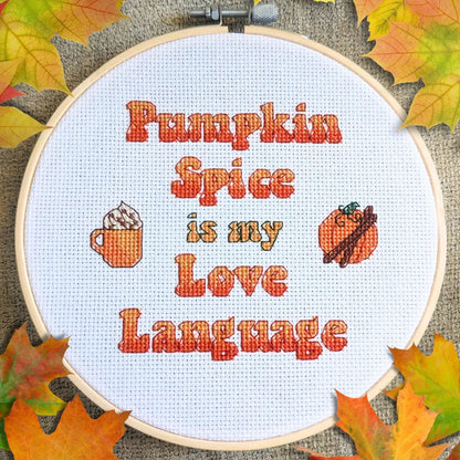 Embroidery hoop with 'Pumpkin Spice is my Love Language' text and fall-themed icons on a textured background with leaves.