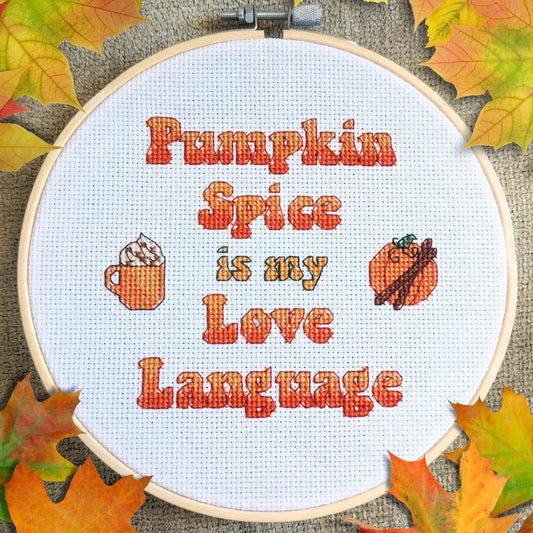 Embroidery hoop with 'Pumpkin Spice is my Love Language' text and fall-themed icons on a textured background with leaves.