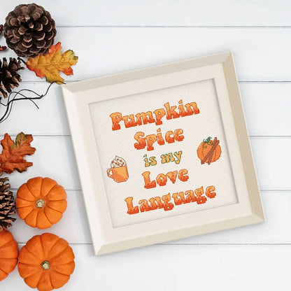 Finished Pumpkin Spice Lover cross stitch by Room for Calm in a cream colored frame on a table with pumpkins, fall leaves, and pinecones