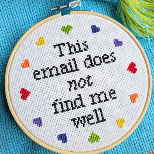 Embroidery hoop with cross-stitched text 'This email does not find me well' on a blue fabric background.