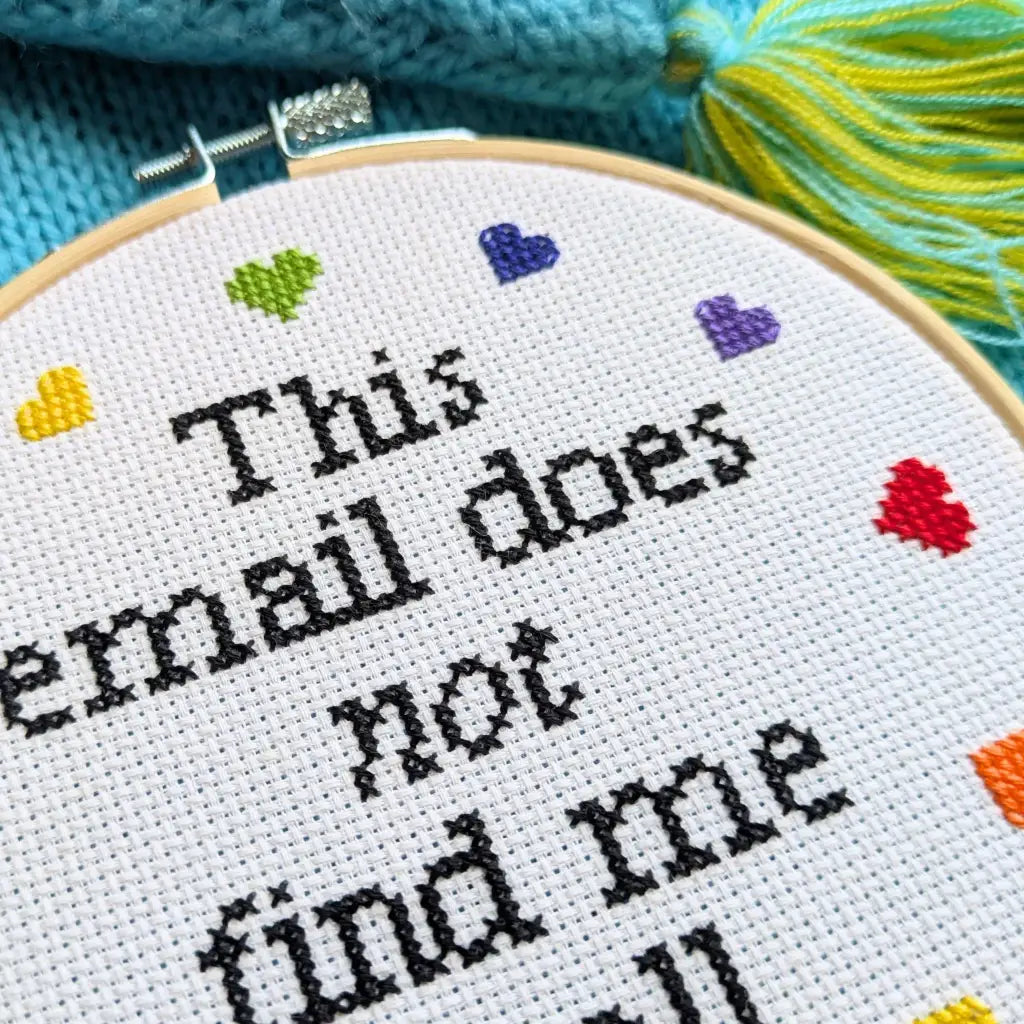 Cross-stitched text in an embroidery hoop with colorful hearts on a blue fabric background