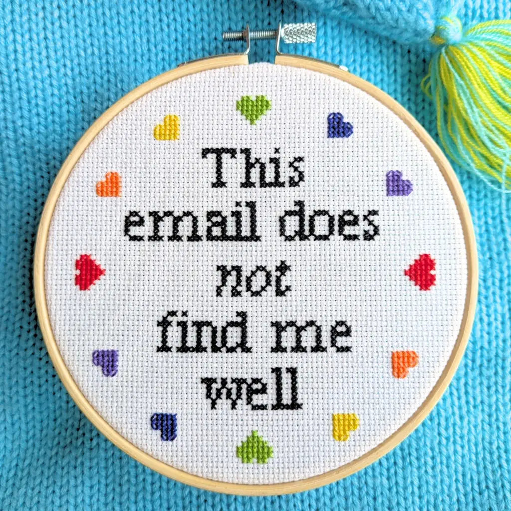 Embroidery hoop with cross-stitched text and colorful hearts on a blue fabric background